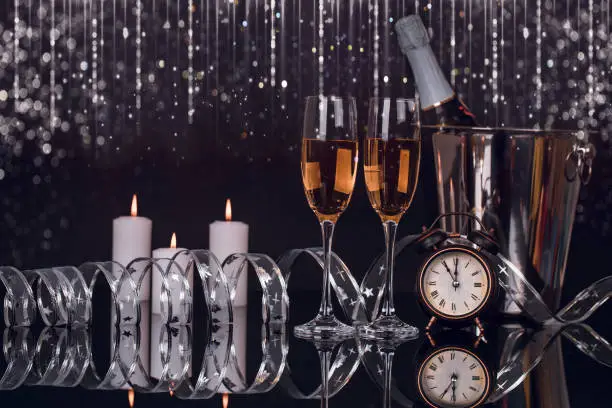 Photo of Two glasses champagne, bottle, clock and Christmas lights