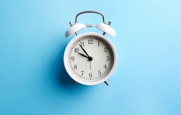 istock White vintage alarm clock on empty blue color background 1081973806