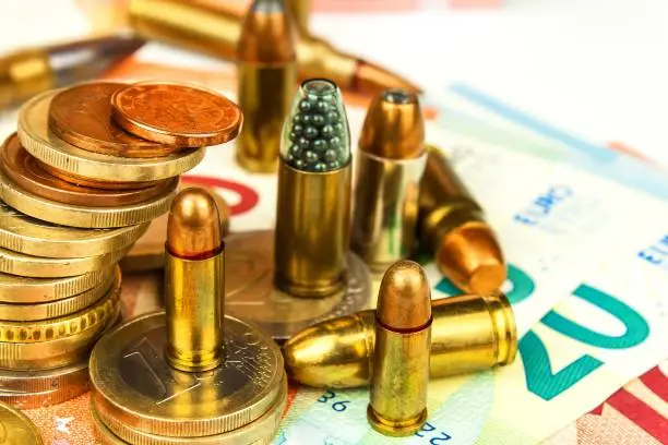 Photo of Euro coins and banknotes and cartridges of different caliber. Illegal trade in ammunition. Sale of weapons. Financing terrorism.