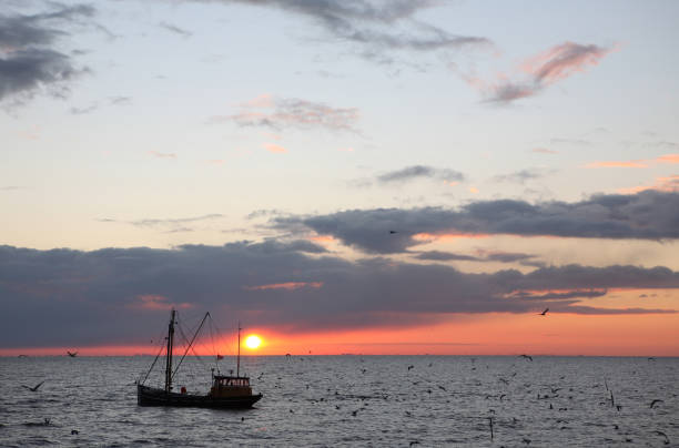 Sun setting behind clouds over calm sea at low tide, creating golden light beams and reflections