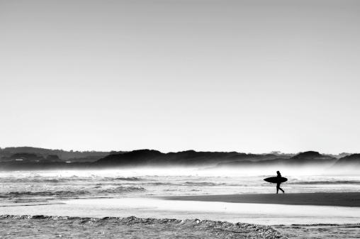 Black and white image of a single surfer heading out towards the waves on Australia's South Coast, famous for its surf.
