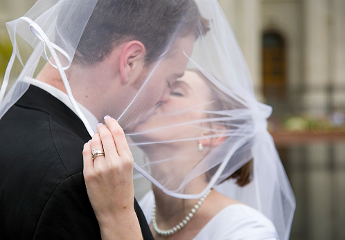 A close up of a bride's hand holding her veil while the couple kisses.