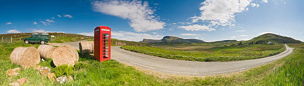 Iconic image of the British countryside with hay bales, bright red phone box and green Land Rover beside a rural lane overlooked by green pasture, mountain peaks and big blue summer skies. ProPhoto RGB color profile for maximum color gamut.