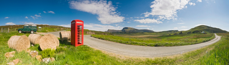 Iconic image of the British countryside with hay bales, bright red phone box and green Land Rover beside a rural lane overlooked by green pasture, mountain peaks and big blue summer skies. ProPhoto RGB color profile for maximum color gamut.