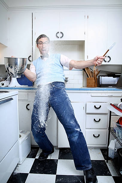 Nerd Trying To Bake Has An Accident The domestic life of a nerdy young man; a baking disaster.  Flour spills through the air and onto the checkered kitchen floor.  Vertical with copy space. flour mess stock pictures, royalty-free photos & images