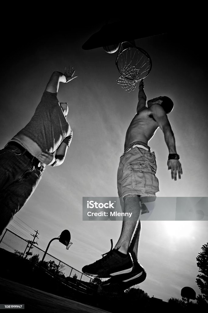 Basketball Dunkin' (Black &amp; White) Dunkin', young basketball players jumping up to the basket on a street court close to sunset. Edited, Masked and Burnt, Black and White. Basketball - Ball Stock Photo