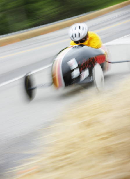 Soapbox Derby Race Car Child Soapbox derby competitor speeds downhill in crouched racing motion blur.  The Soap Box Derby is a youth car racing program which has been run in the United States since 1934. World Championship finals are held each July at Derby Downs in Akron, Ohio. Race cars are unpowered, relying entirely upon gravity to move downhill.  Early cars were constructed of wood from crates and other scrap sources, with wheels from baby buggies and wagons.  Today, using standardized wheels with precision ball bearings, modern racers start on a ramp at the top of a hill, and attain speeds of up to 35 miles per hour.  Irondequoit, New York, 2008. soapbox cart stock pictures, royalty-free photos & images