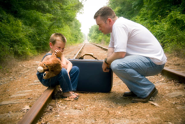 istock Man Talking to Little Boy Sitting on Tracks with Suitcase 108200564