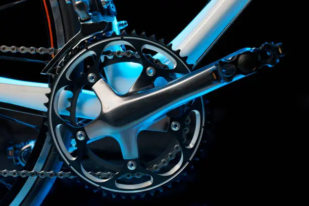 Pedal, crank, front sprockets and derailleur shot in cool light in the studio. The bike is a brand-new top model worth thousands of dollars.