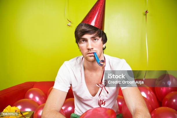 Grave Joven Usando Gorro De Fiesta Con Globos Soplando Bocina Foto de stock y más banco de imágenes de Fiesta