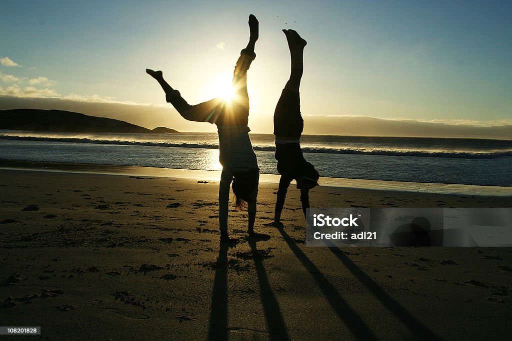 Silueta de dos mujeres haciendo hacer el pino en la playa al atardecer - Foto de stock de Mujeres libre de derechos