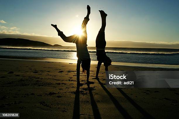 Sylwetki Dwóch Kobiet Robi Pompki W Staniu Na Rękach Na Plaży O Zachodzie Słońca - zdjęcia stockowe i więcej obrazów Kobiety