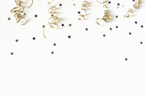 Happy New Year or birthday festive composition. Golden confetti and glittering stars on white table background. Celebration, party concept. Flat lay, top view, empty copy space.
