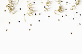 Happy New Year or birthday festive composition. Golden confetti and glittering stars on white table background. Celebration, party concept. Flat lay, top view. Empty copy space.
