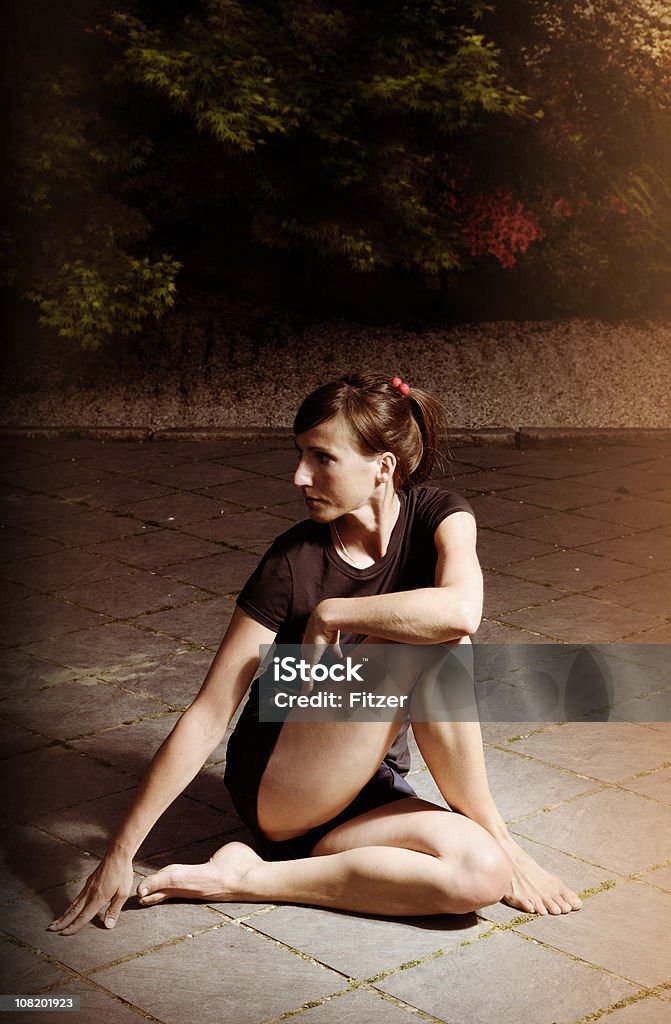 Giovane donna seduta all'aperto, sulla terrazza e Stretching - Foto stock royalty-free di Abbigliamento sportivo