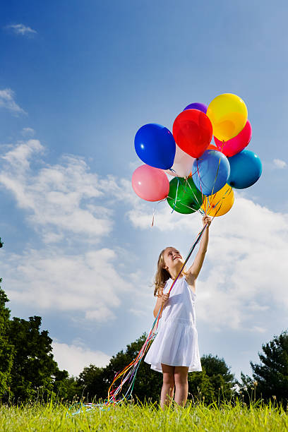 Little girl looks up at balloons held aloft stock photo