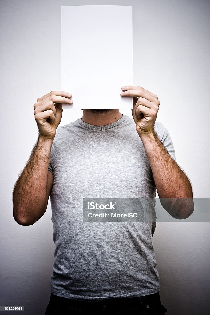 Hombre que agarra hoja de papel blanco en frente de la cara - Foto de stock de Cara oculta libre de derechos