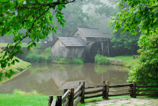 An historic grist and lumber mill located on the Blue Ridge Parkway sits alongside a pond enshrouded by fog on a late afternoon day.