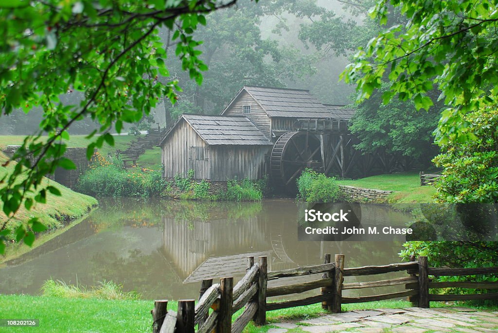Mabry Mill on edge of pond An historic grist and lumber mill located on the Blue Ridge Parkway sits alongside a pond enshrouded by fog on a late afternoon day. Watermill Stock Photo