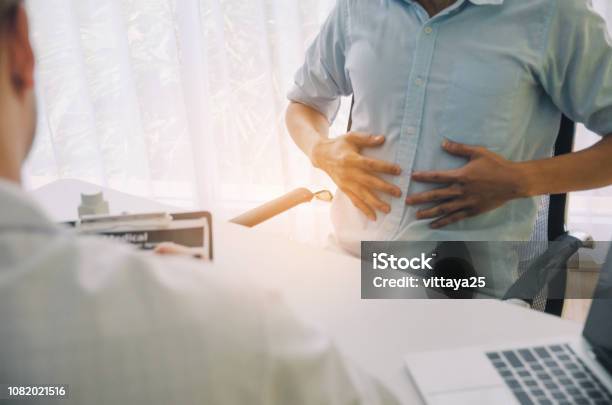 Foto de Jovem Sofre De Dor De Estômago Encontrar Médico Prescrevendo Receita Na Área De Transferência Com O Laptop Na Mesa Num Hospital Síndrome De Escritório Cuidados De Saúde Médicos Medicina Conceito De Farmácia e mais fotos de stock de Abdome