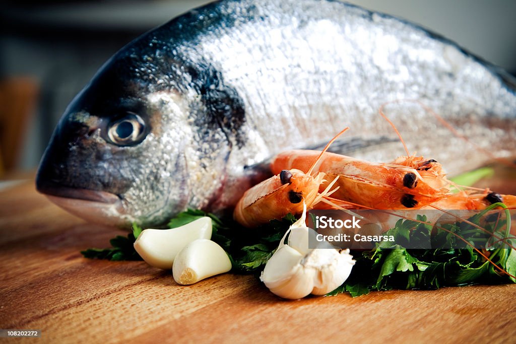 Pesce e gamberi seduto sul Tagliere con aglio - Foto stock royalty-free di Aglio - Alliacee