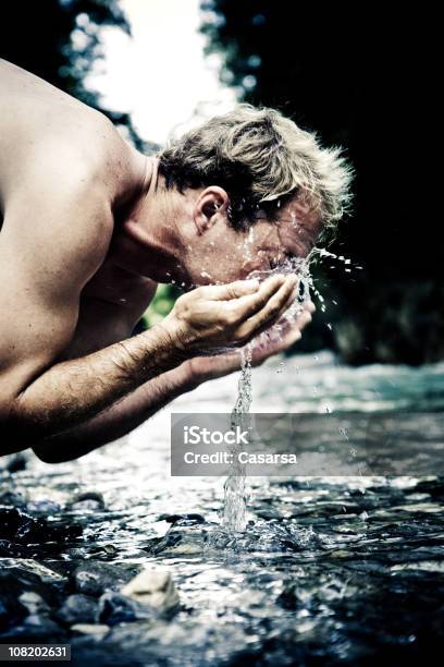 Young Man Leaning Over River And Splashing Water On Face Stock Photo - Download Image Now