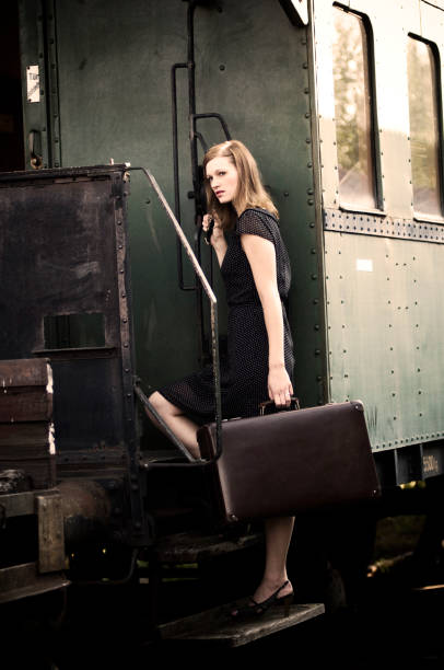 Female brunette traveler with red suitcase in white skirt waiting for a train and waving hand to the train on raiway station