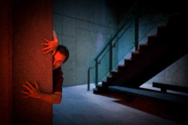 Man in a sweatshirt with a black hood looks at a hole in a metal fence. Teenager in a depressed, hopeless state, a state of stress withdrew into himself, hid under a hood.