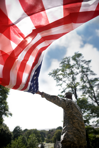 American Soldier holding a United States flag with the sun shining through. Focus on flag. Copy space.