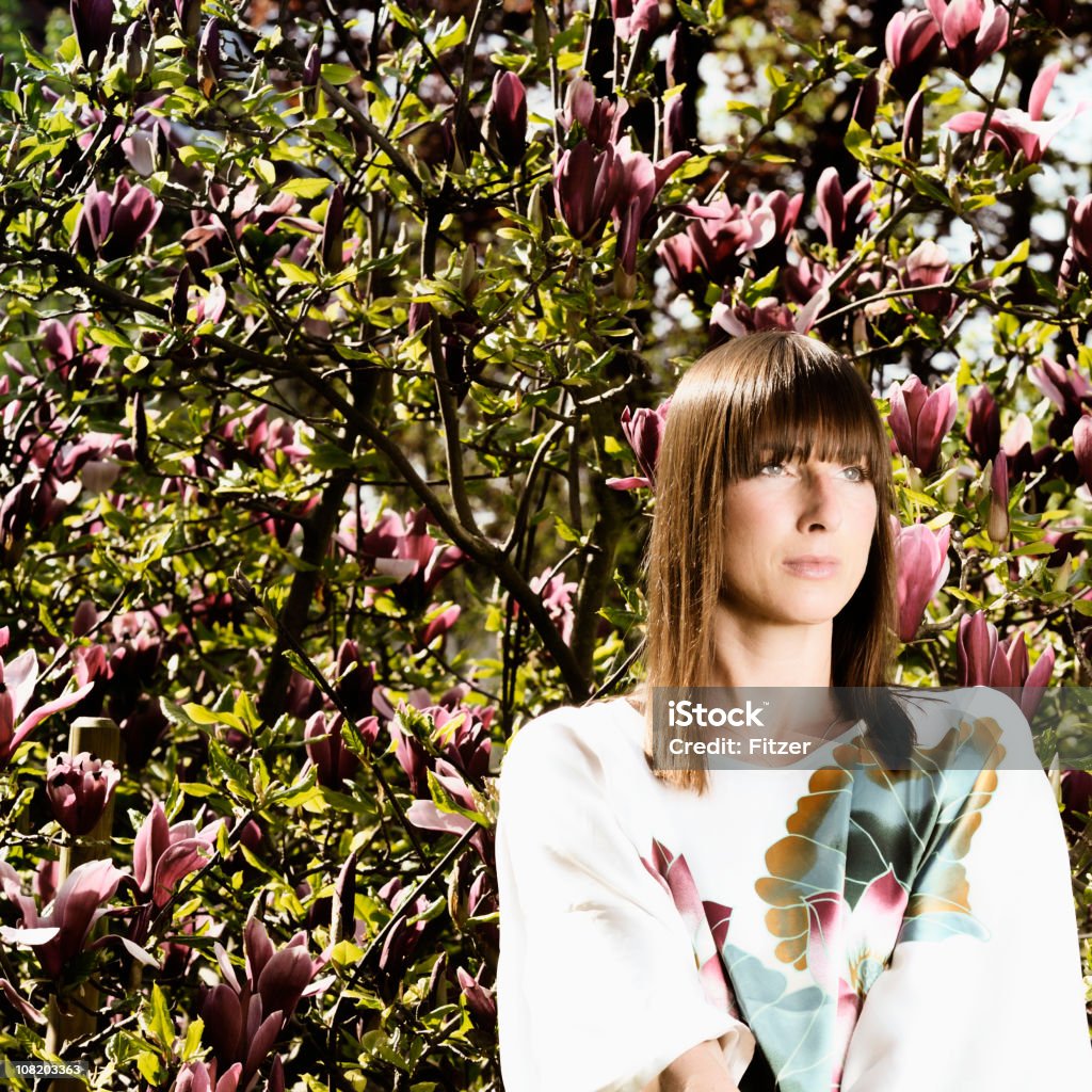 Mujer joven de pie cerca de árbol con flores - Foto de stock de Adulto libre de derechos