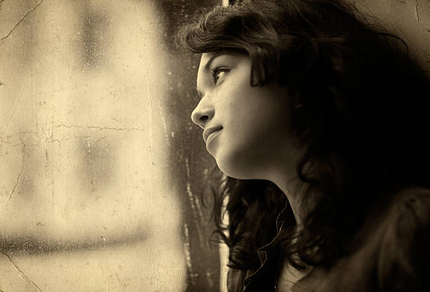 Sepia Toned Portrait of Pensive Young Woman Looking Out Window stock photo