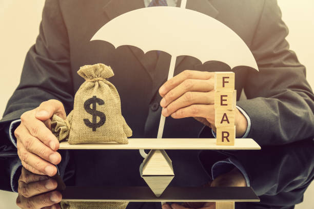 Fear and greed or anxiety in financial market concept : Businessman carries a white umbrella, protects dollar bags or properties on basic balance scale, depicts the influence of emotions on investors miedo y la codicia o ansiedad en el concepto de mercado financiero: hombre de negocios lleva un paraguas blanco, protege dólar bolsas o propiedades a escala de equilibrio básico, representa la influencia de las emociones sobre los inversores