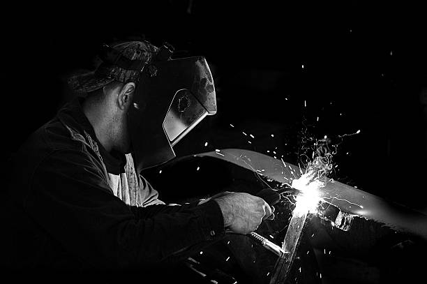 Man Welding, Black and White A photo of a man welding. welding helmet stock pictures, royalty-free photos & images