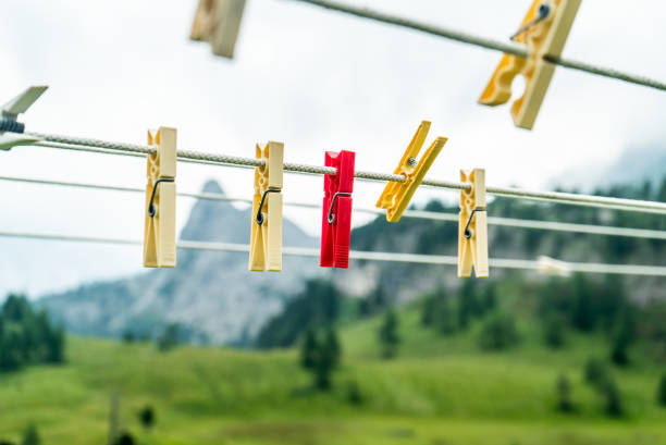 Clothes pins on a clothes line rope. clothespins hanging hook. Clothes pins lined up on a wire. Fresh green meadow and mountains on the background. Wooden clothes pins on a string outside laundry