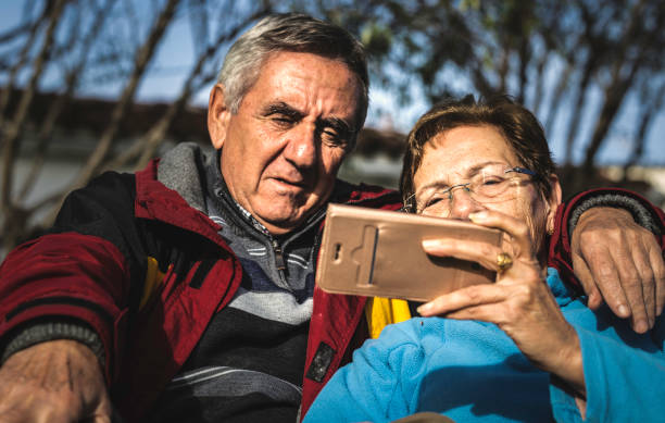 istock Mature woman with smartphone embraced by her husband while both sitting in park 1082044634