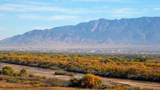 A view from the west mesa of the Rio Grande, cottonwood trees in the Bosque (Spanish for woods), and the city of Albuquerque at the base of the Sandia mountains, part of the Rocky Mountain chain in the Southwest, USA.