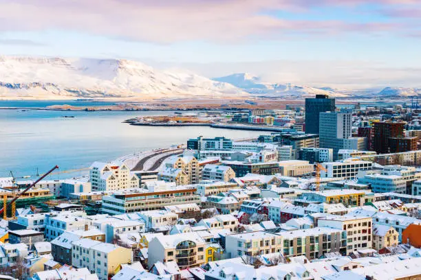 This is a color photograph of downtown Reykjavik, Iceland seen from a high angle view on a winter morning. The building rooftops are covered in snow.