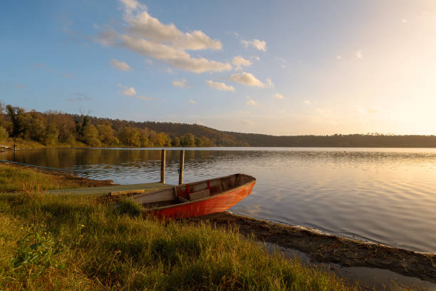 Beach on Lake Martignano, with boat moored on the shore, in the first area. The light of the sunset is reflected on the lake.