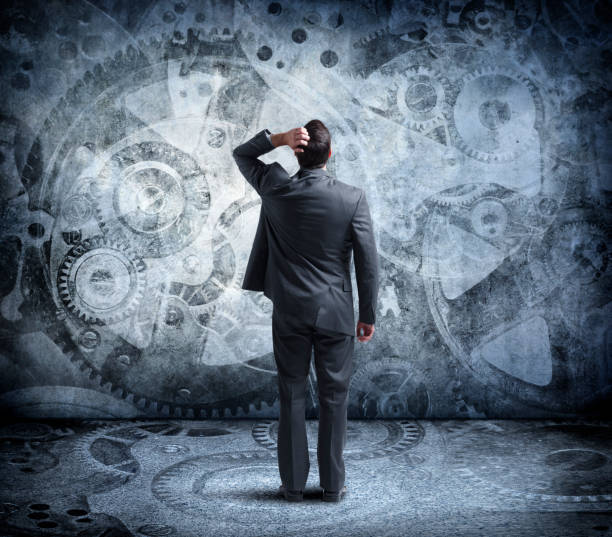 istock Man Looks Up At Confusing Array Of Large Interlocking Gears On Wall In Front Of Him 1082087682