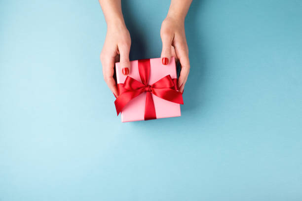 istock Female hands holding gift box on blue background. 1082089582