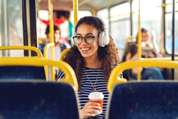 muchacha sentada ventana de ina un autobús tomando café, escuchando música y mirando a través. - transporte público fotografías e imágenes de stock