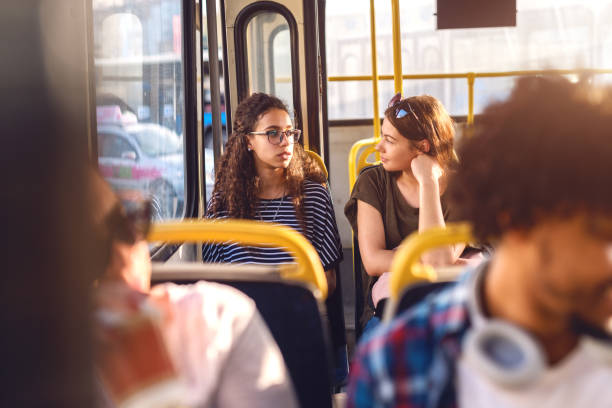 due amici seduti su un autobus, che parlano guardando la finestra del trogolo. - transportation bus mode of transport public transportation foto e immagini stock