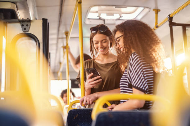 deux jeunes filles regarder téléphone et souriant tout en se tenant debout sur un bus. - public transportation photos photos et images de collection