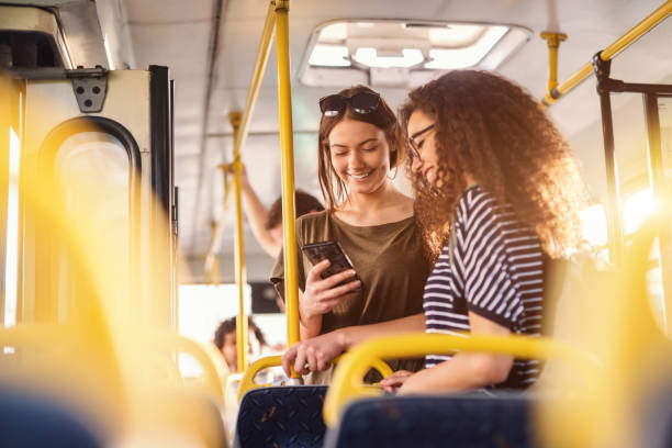 携帯電話を見て、ニコニコとバスに立っている二人の女の子。 - commercial land vehicle 写真 ストックフォトと画像