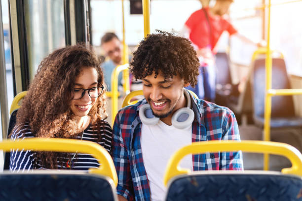 istock Young multicultural couple looking down and smiling while sitting and riding in city bus. 1082096704