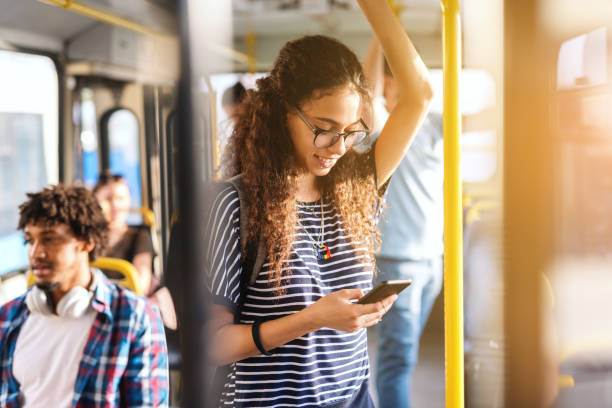 istock Beautiful mixed race girl with long curly hair using smart phone for reading or writing message while standing in city bus. 1082096802