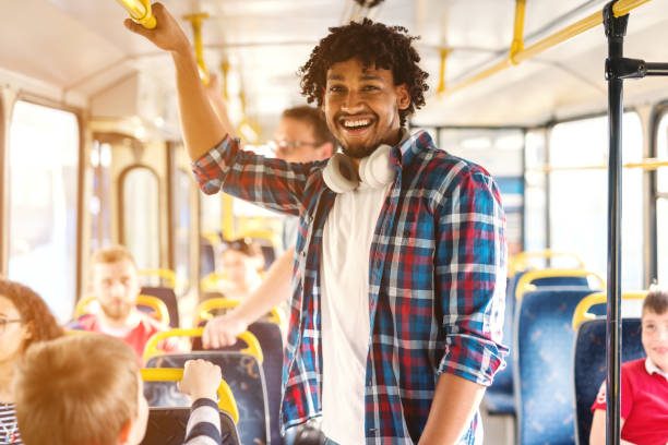 giovane afroamericano sorridente che cavalca sull'autobus urbano e guarda la telecamera. - bus transportation indoors people foto e immagini stock