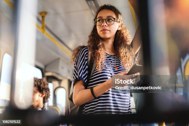 Beautiful Mixed Race Girl With Long Curly Hair Using Smart Phone For Reading Or Writing Message While Standing In City Bus Stock Photo - Download Image Now