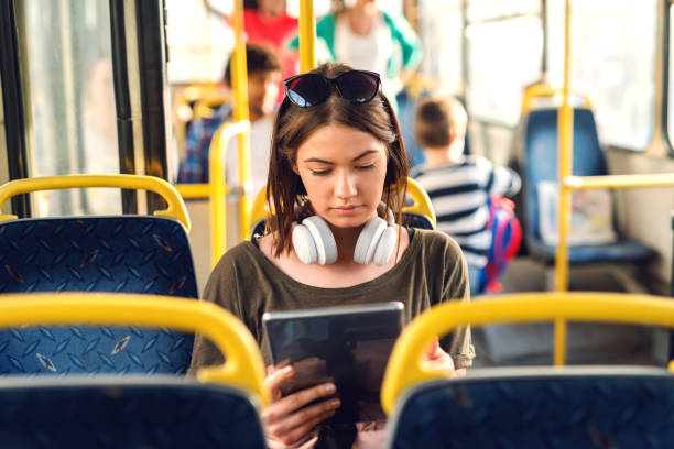 バスの中で座って、タブレットを見てヘッドフォンでかなり若い女の子。 - time zone audio ストックフォトと画像