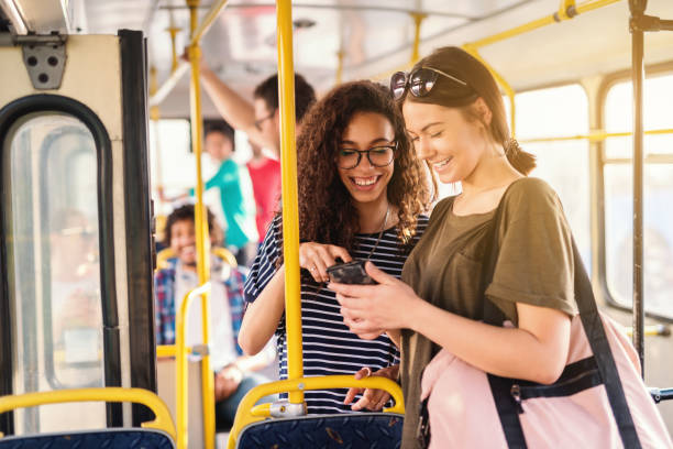 dos amigos riendo y mirando el teléfono esperando bus para salir. - depart fotografías e imágenes de stock